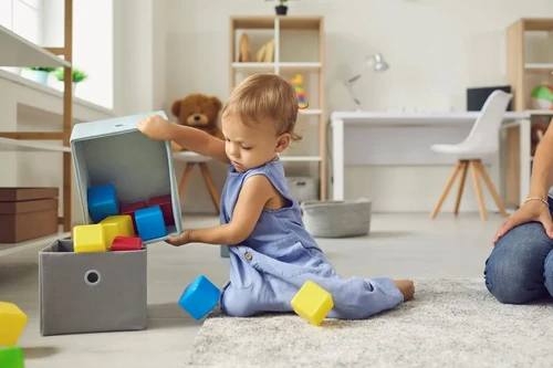 A toddler puts blocks back into their toy storage box