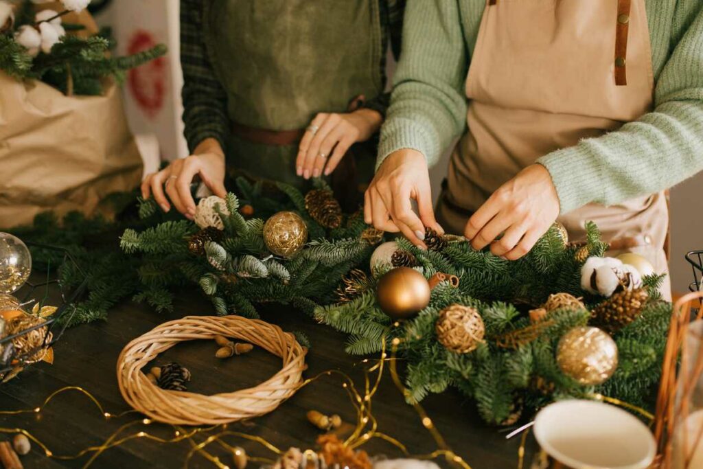 Close-up shot of two women making winter decorations on a wooden table.