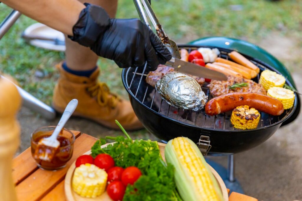 Closeup of a man cooking meat and vegetables on an outdoor grill.